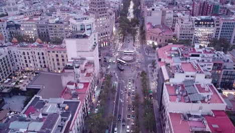 Calles-De-Barcelona-Con-Tráfico-Al-Atardecer,-Luces-De-La-Ciudad-Empezando-A-Brillar,-Vista-Aérea