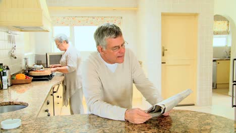 mature man reading a newspaper in the kitchen