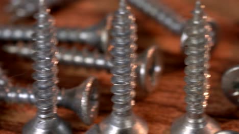 the bunch of steel screws on wooden table. screw production, heap of metal details, close up shot