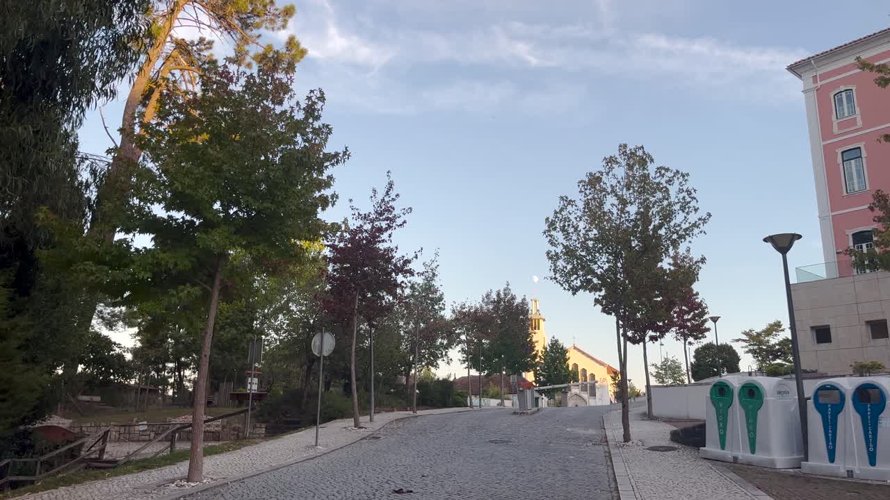 Daytime capture of city's empty street with low angle sunlight, park walking area with trees on one side and residential building on other
