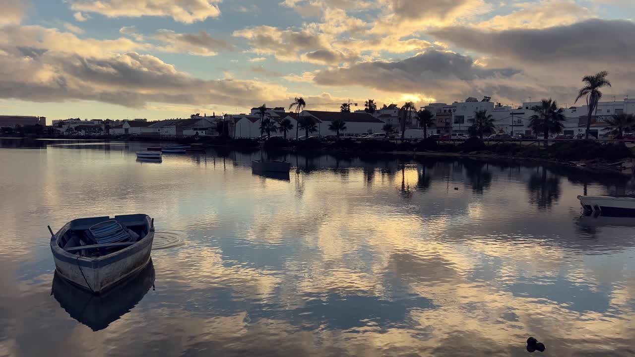 작은 목조 시 배는 화려한 일몰 중에 스페인 바르바테의 평온한 물 위에 부드럽게 떠다니고 있습니다.