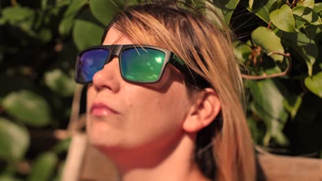 a woman in sunglasses rests in a wooden chair on a terrace