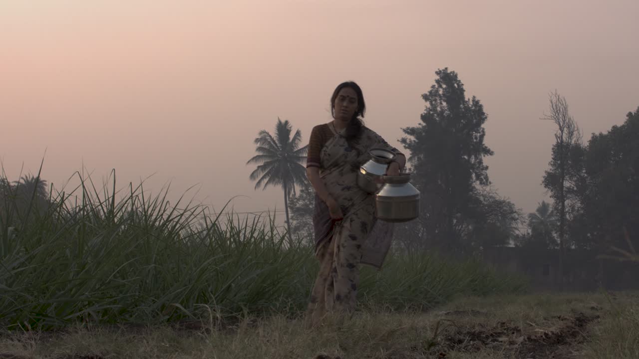 Indian woman walking to the camera with jars at sunset