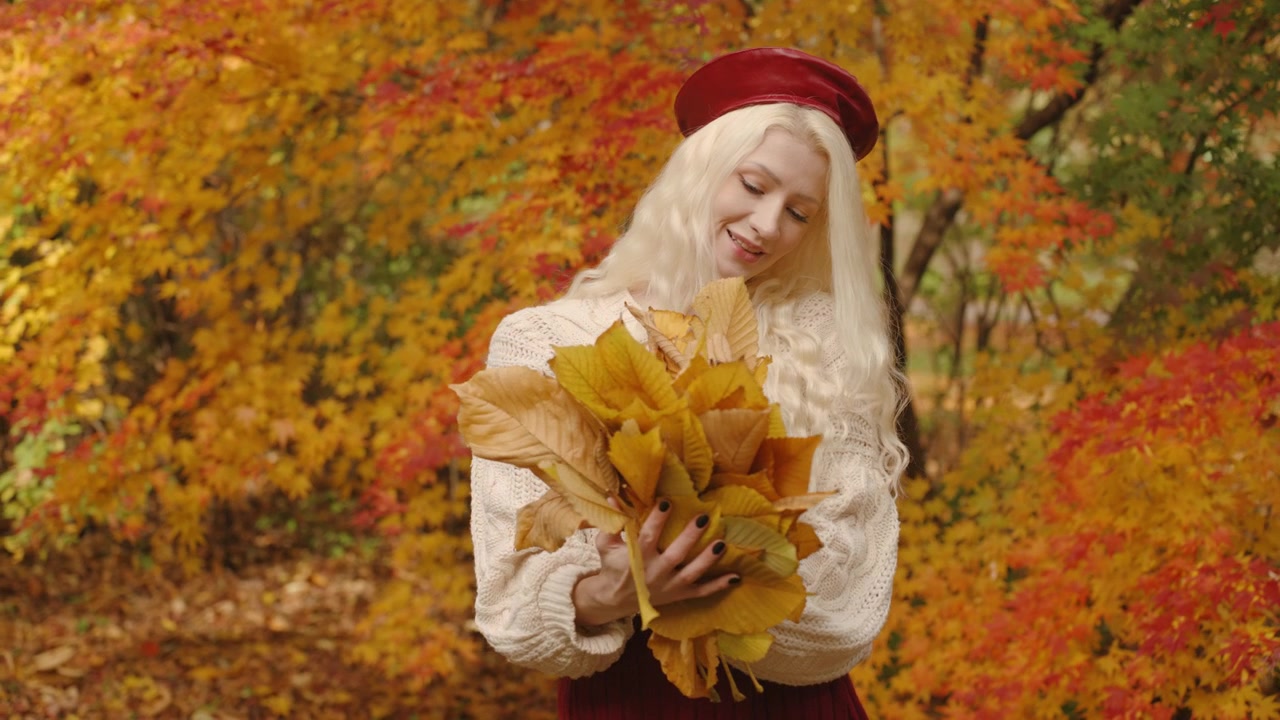 Donna bionda che tiene in mano foglie autunnali di castagno colorate nel Forest Park, circondata da un vibrante e caldo fogliame autunnale rosso, slow motion.