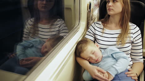 tired woman in the train with sleeping son on her lap