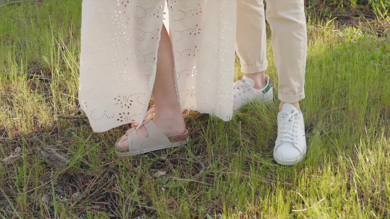 close up of couple's feet on grass at sunset one in sandals one in white sneakers