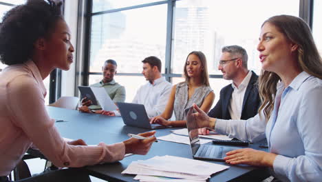 multi-cultural business team meeting around office boardroom table with laptops discussing documents