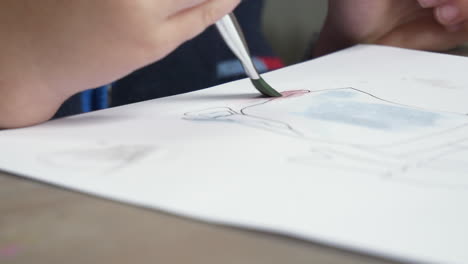 close up of a young boys hand and watercolour brush, painting in a pre drawn figure