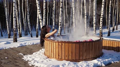 relaxing in steaming hot tub, woman enjoys serene winter landscape with snow covered birch trees, embodying tranquil wellness and peaceful winter retreat