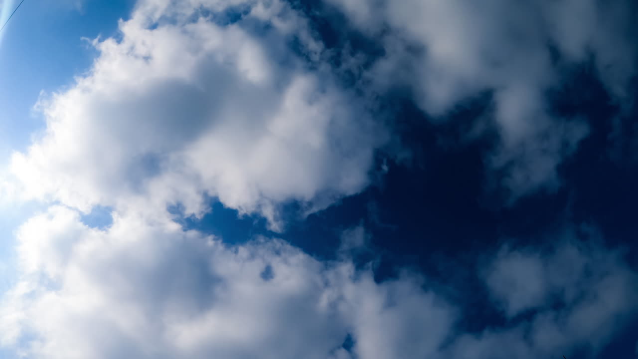 Deep blue sky hardly seen behind the quickly flying white clouds. Low angle view on the cloudscape timelapse.