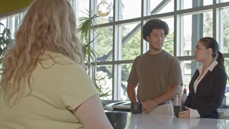 three workers in their 20's talking in an office setting with a senior citizen worker walking by with video dolly right to left