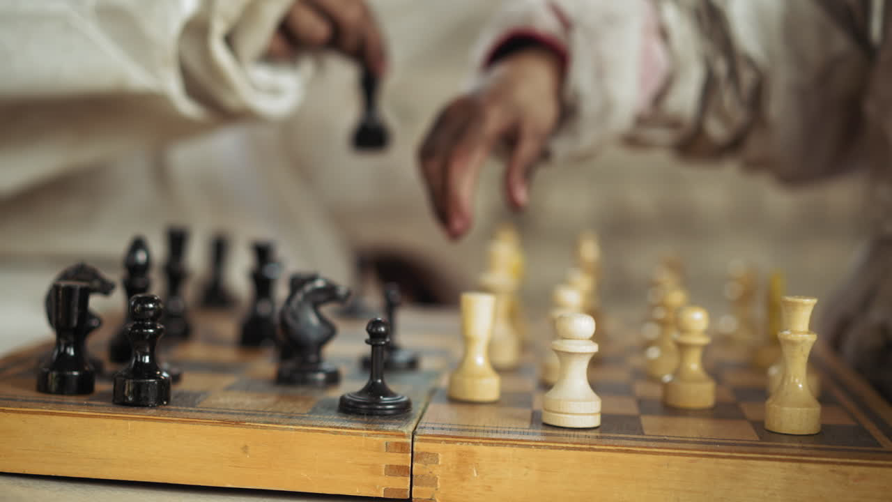 Close up of hand placing white chess piece on wooden board during strategic match, surrounded by focused black and white chessmen, illustrating decision making