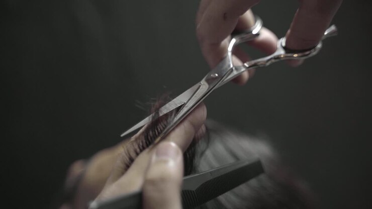 Primo piano di un parrucchiere che pettina e taglia i capelli di un uomo con le forbici