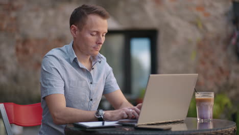 A-serious-man-is-a-business-student-working-studying-sitting-at-a-table-and-typing-a-message-on-a-laptop.-Typing-text-on-the-keyboard