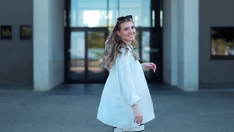 Beautiful-young-small-woman-running-towards-modern-building-and-smiling-at-camera