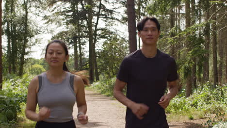 mid adult couple exercising doing work out outdoors running along track through forest towards camera wearing sports clothing 5