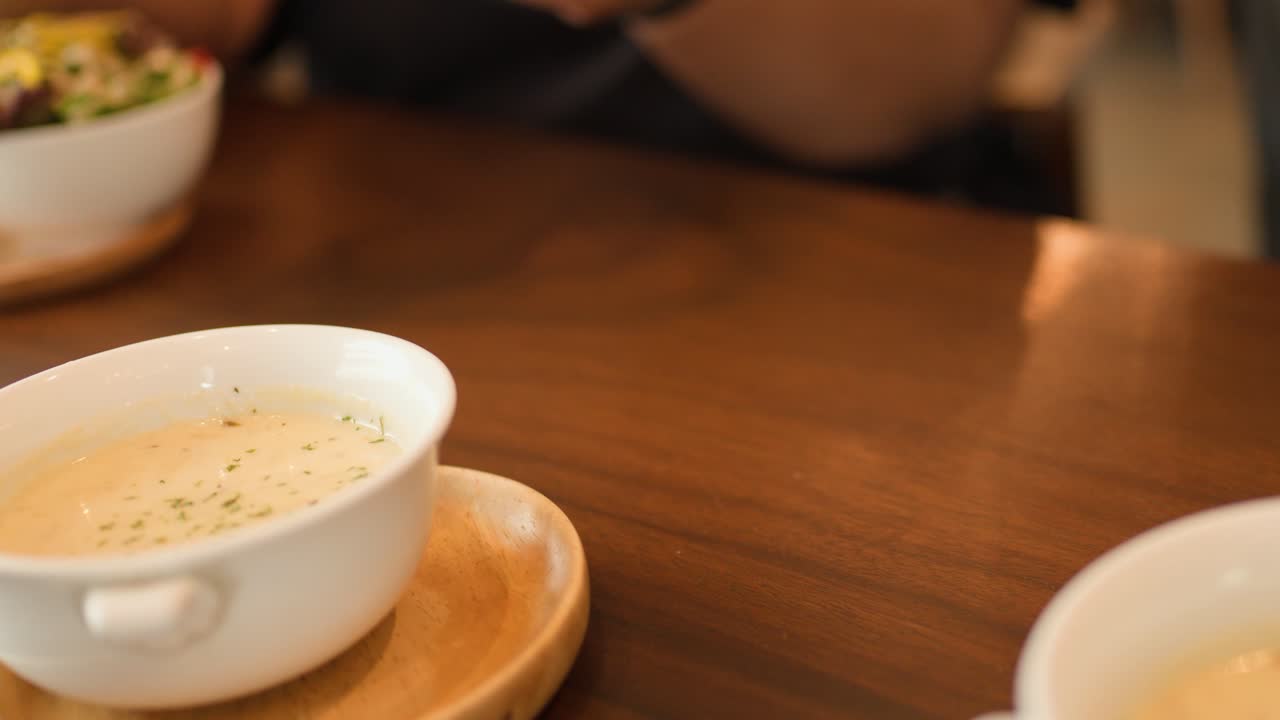 Hand sets creamy soup bowl on wooden plate in warmly lit, casual cafe setting
