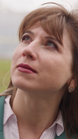 peaceful woman with long hair waving in light wind looks upward at highrise building against car driving by. lady examines city architecture closeup slow motion