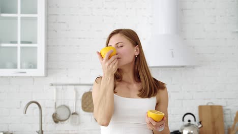 a cheerful girl covers her eyes with orange slices. emotions in the white kitchen. healthy eating