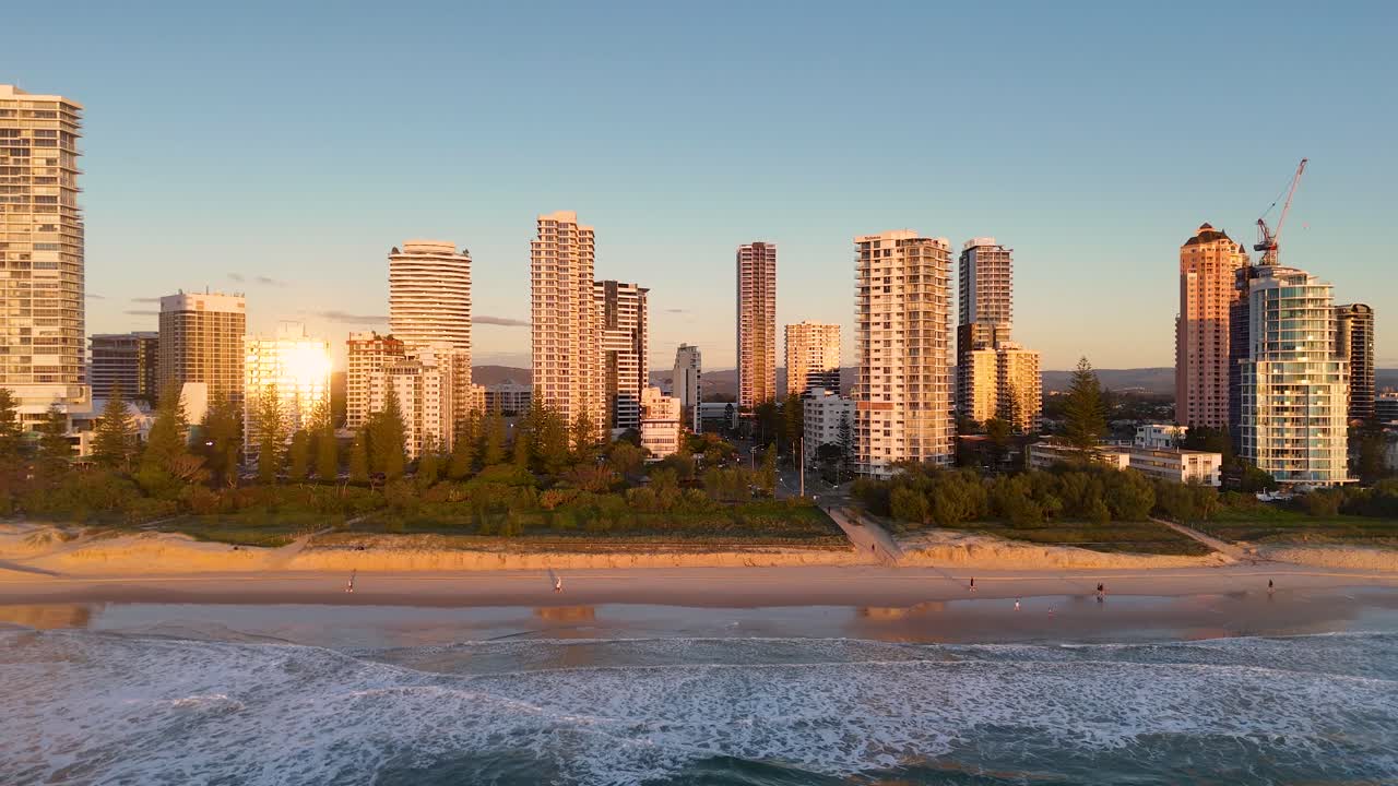 Aerial view of Gold Coast's skyline at sunrise, highlighting skyscrapers and beach with warm morning light reflections