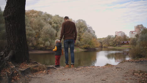 un hombre con su hijo pequeño están admirando la belleza del lago forestal en un día de otoño viajando y descansando en la naturaleza en el otoño vista de atrás del padre y el hijo