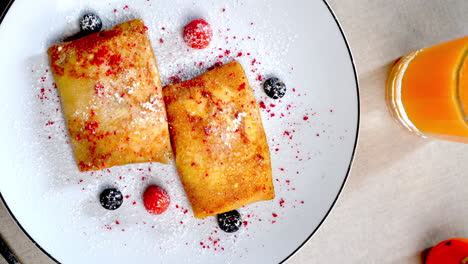 two golden pancakes are served on a white plate. garnished with raspberries. blackberries. and a sprinkle of powdered sugar. possibly representing a traditional eastern european breakfast or dessert