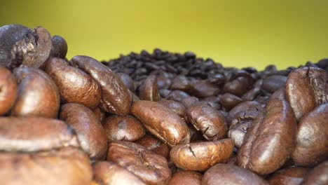 Slow-zoom-out-shot-of-roasted-coffee-beans-falling-down-in-slow-motion-in-front-of-yellow-background