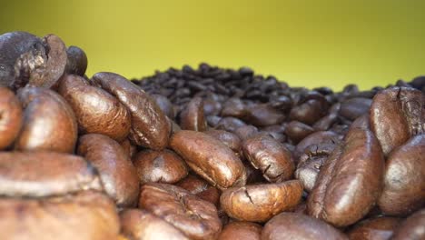 alejamiento lento de una toma de granos de café tostados cayendo en cámara lenta frente a un fondo amarillo