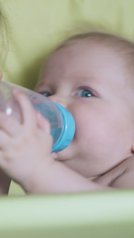 careful elder sister gives to drink water to adorable little boy sitting in soft highchair in light room