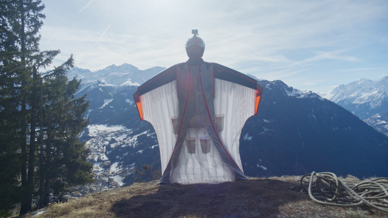 Wingsuit BASE jumper flying over Verbier surrounded by alpine mountains with snow-covered peaks. High-speed flight, dramatic scenery, and cinematic extreme sports action in the Swiss Alps.