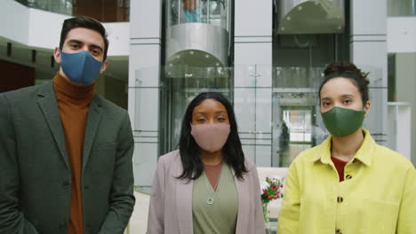 equipo de negocios multiétnico con máscaras posando para la cámara en el centro de la oficina