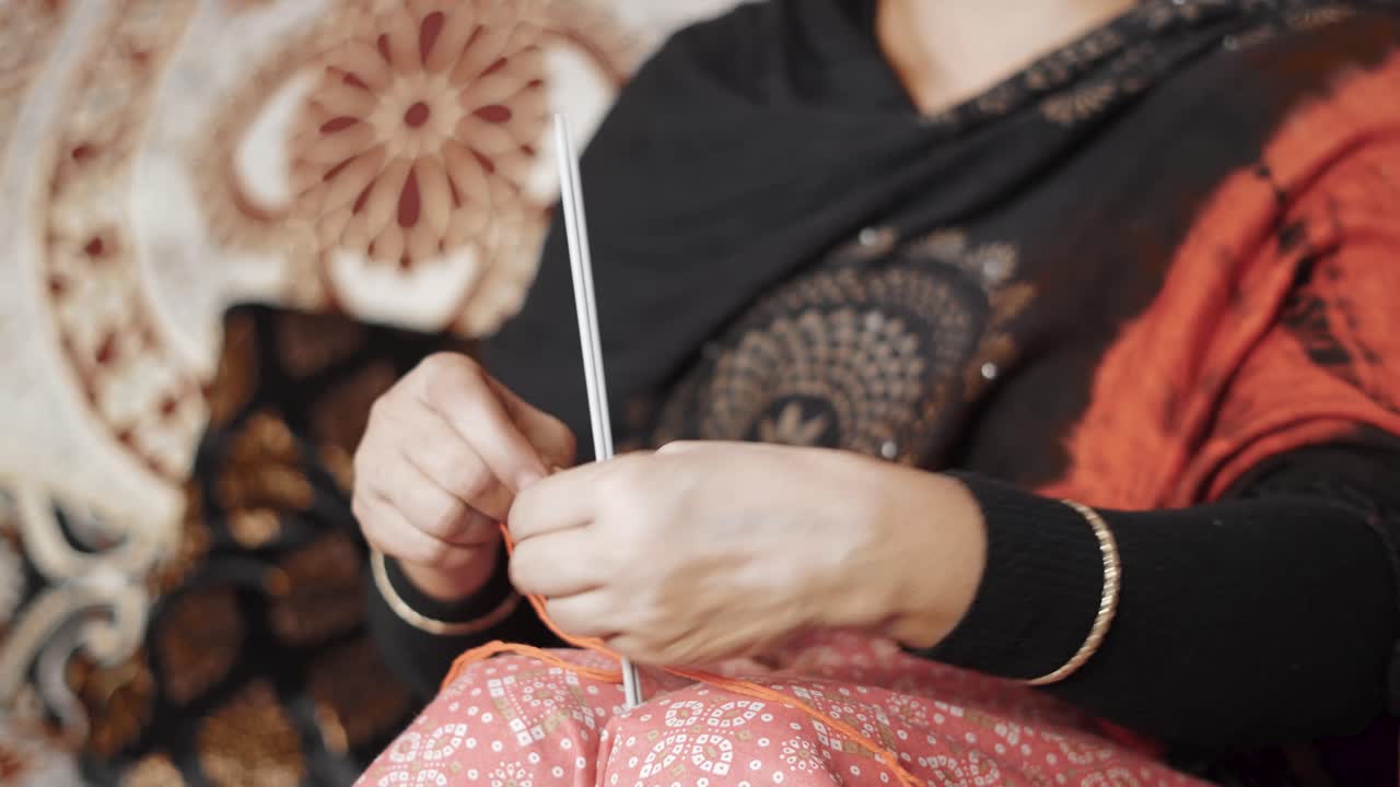 전통적인 인도 여성은 붉은 실과 바늘 공예로 뜨개질을 시작합니다.