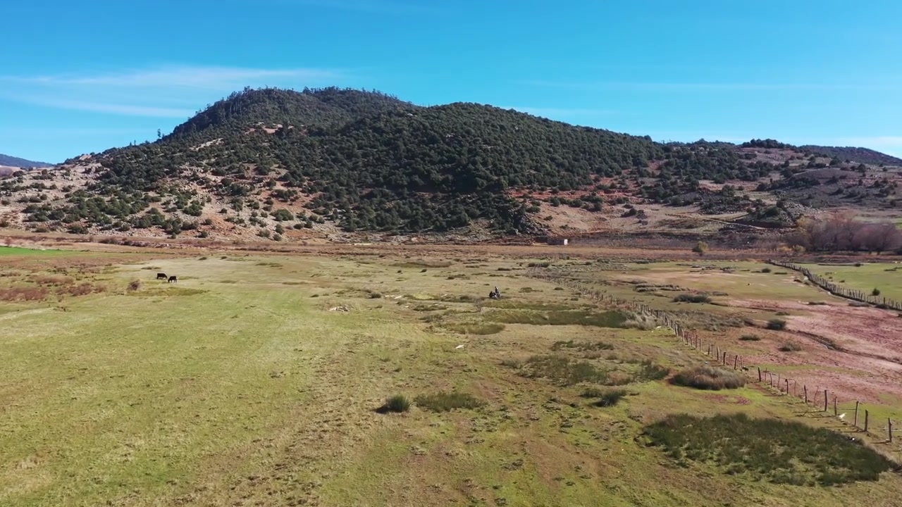 Vista aérea de drone de pastagens abertas e colinas ondulantes num vale marroquino tranquilo com paisagem rural natural sob um céu azul brilhante.