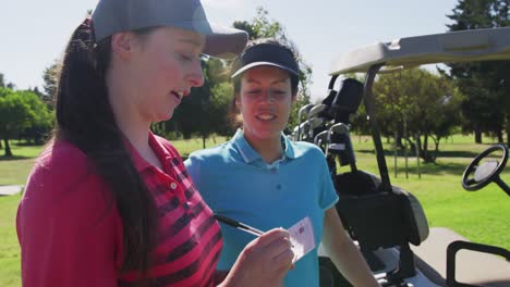 Zwei-Kaukasische-Frauen-Spielen-Golf,-Eine-Schreibt-In-Ein-Notizbuch