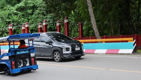 tuk-tuk and car passing on a colorful road