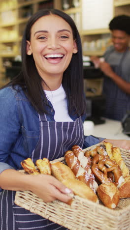 barista biracial sonriente en delantal sostiene la canasta de la panadería en la cafetería