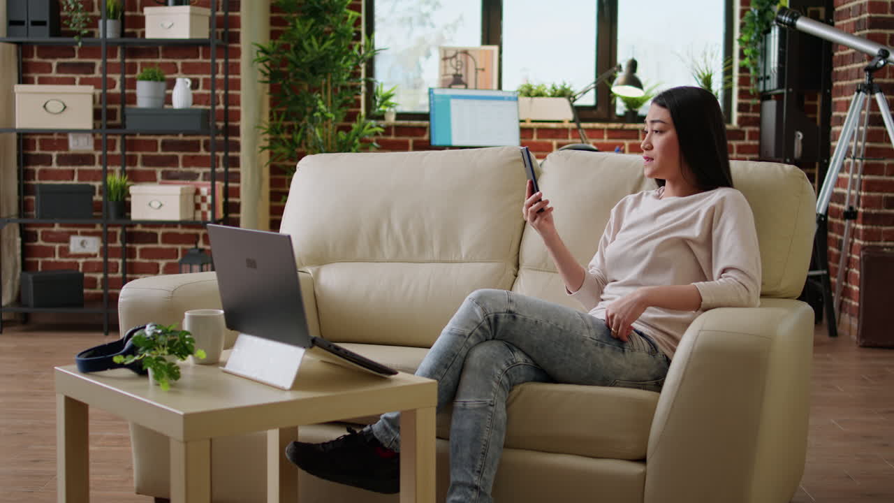 Woman using smartphone and laptop on couch in living room
