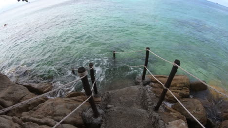 toma pov bajando las escaleras de las rocas costeras rodeadas de hermosas aguas azules claras