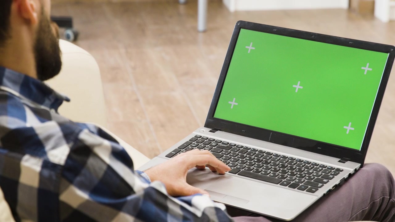 Uomo che usa il laptop con schermo verde in soggiorno.