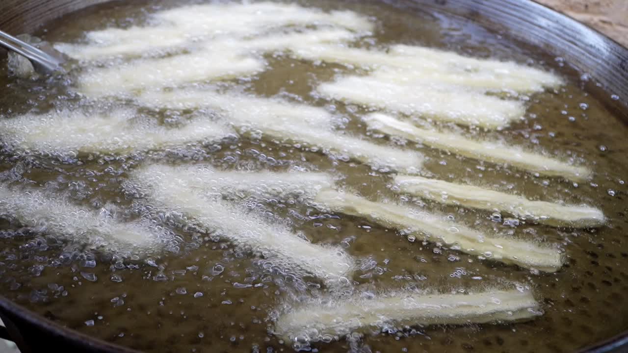 Closeup of churros being cooked in boiling oil.