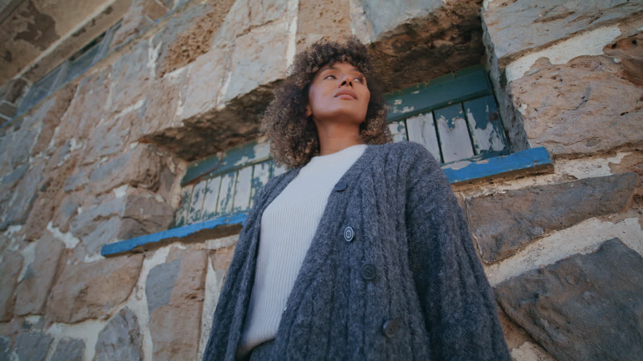 Serene woman looking camera standing near rocky wall bottom view. Curly lady