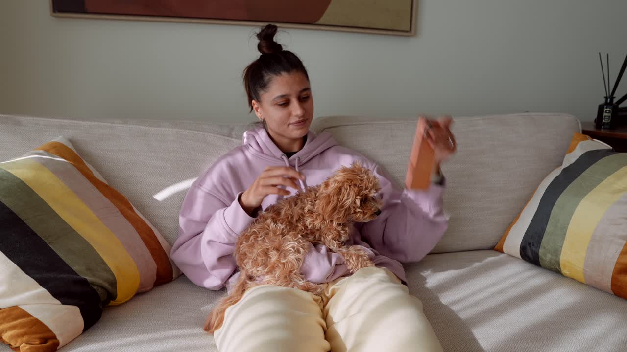 Young Woman Cuddling Puppy and Using Phone on Sofa