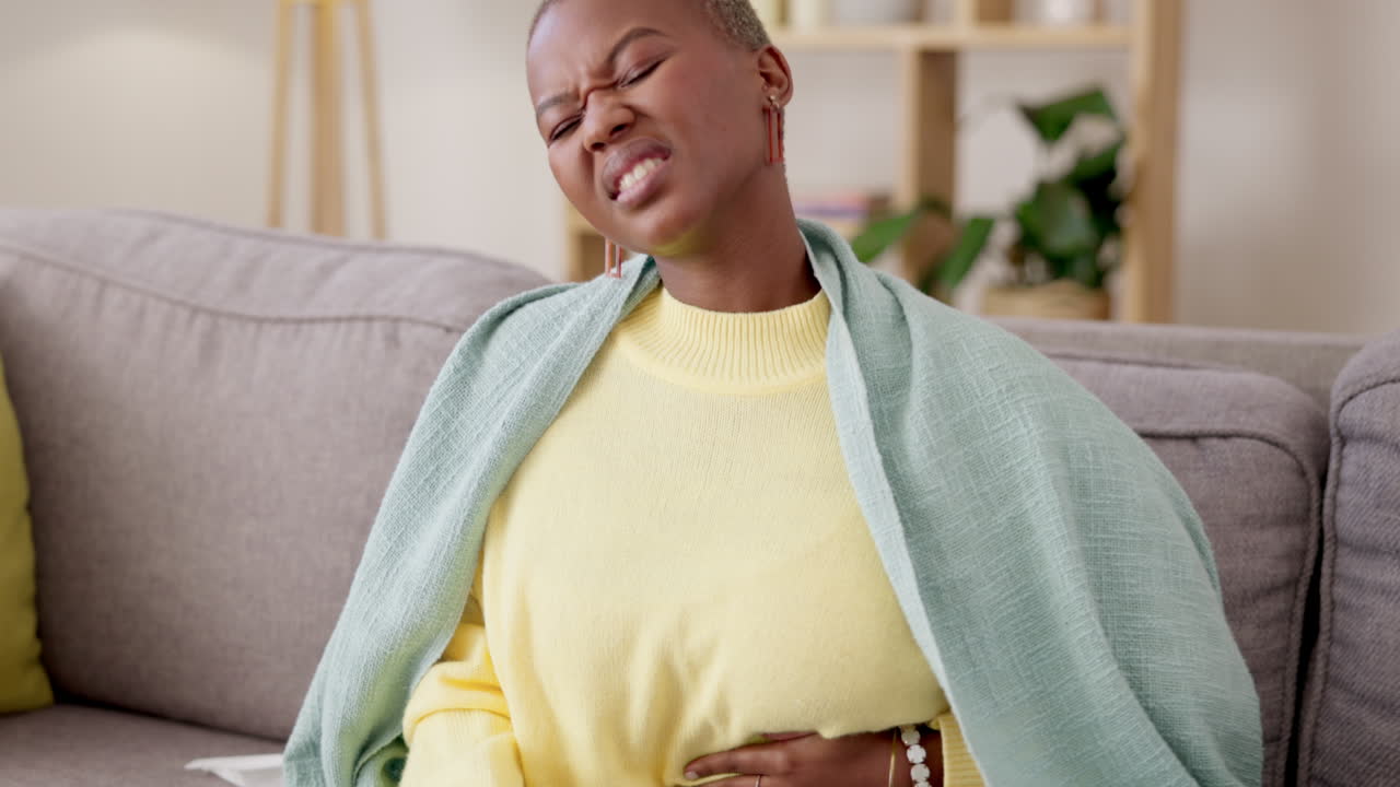 Black woman, couch and stomach with cramp