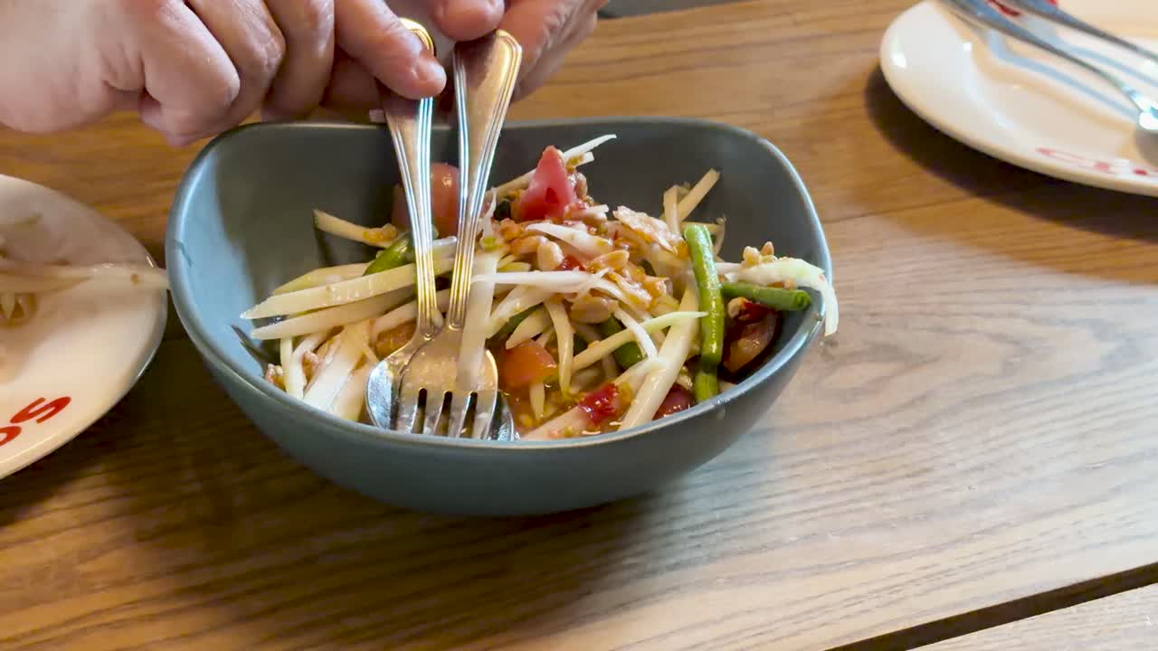 Hands mix som tum salad in natural light, wooden table, close-up, steady camera, casual mood