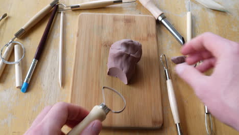 close up on the hands of an artist or sculptor cutting and carving a strangely satisfying soft brown modeling clay sculpture with a tool