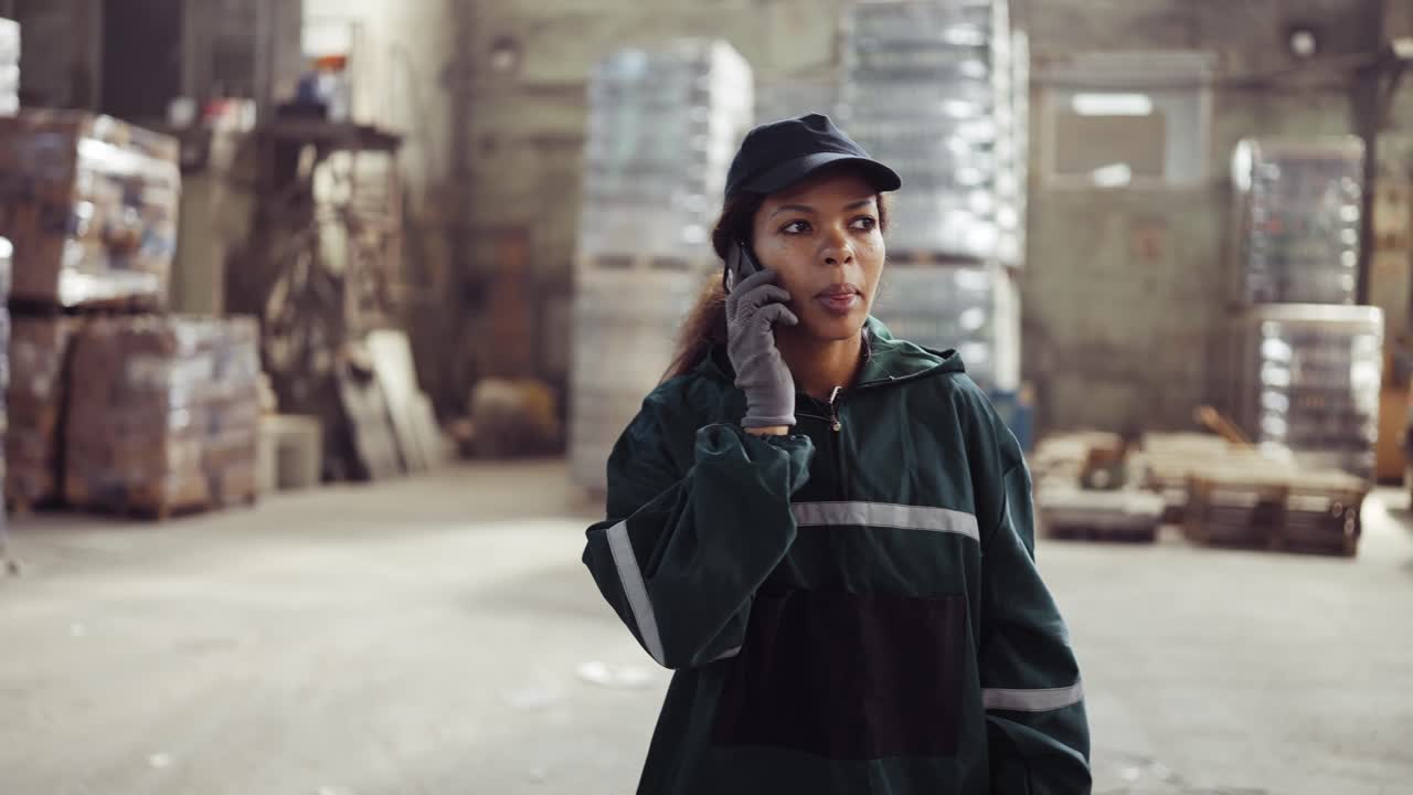 an African American woman in a special green uniform speaks on the phone at a waste processing plant. Factory background. Processing of raw materials, recycling. Pollution control