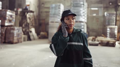 an african american woman in a special green uniform speaks on the phone at a waste processing plant. factory background. processing of raw materials, recycling. pollution control