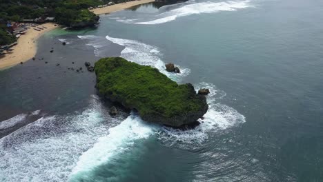 orbit drone shot of coral rocks in the middle of the beach hits by the sea wave