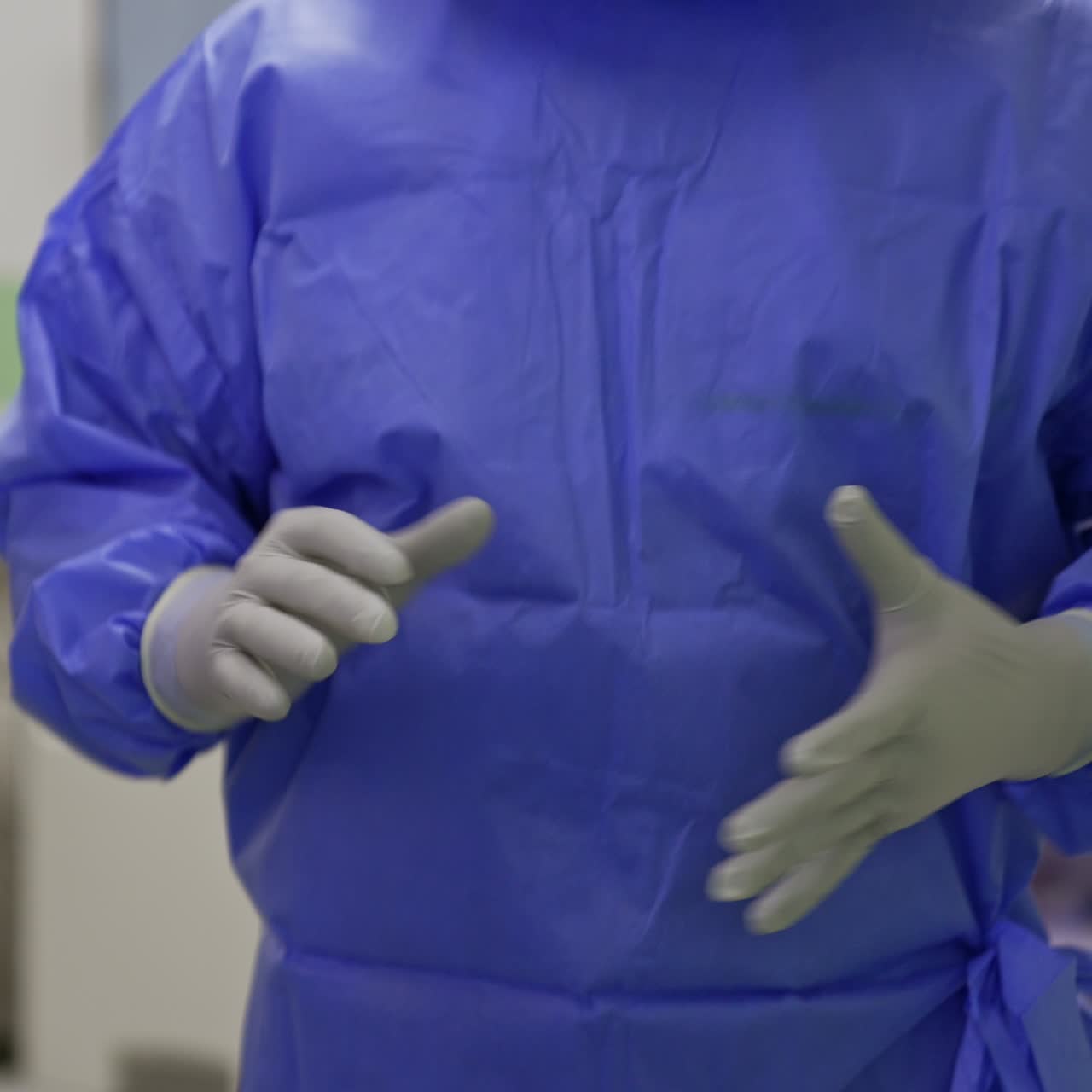 Nurse helping the doctor to put on the second pair of latex gloves. Surgeon in protective outfit is ready for surgery