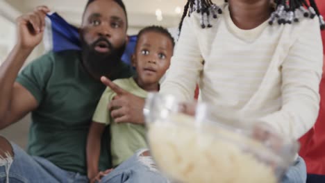 Afroamerikanische-Eltern-Mit-Sohn-Und-Tochter,-Die-Zu-Hause-Sport-Im-Fernsehen-Mit-Flagge-Schauen,-Zeitlupe